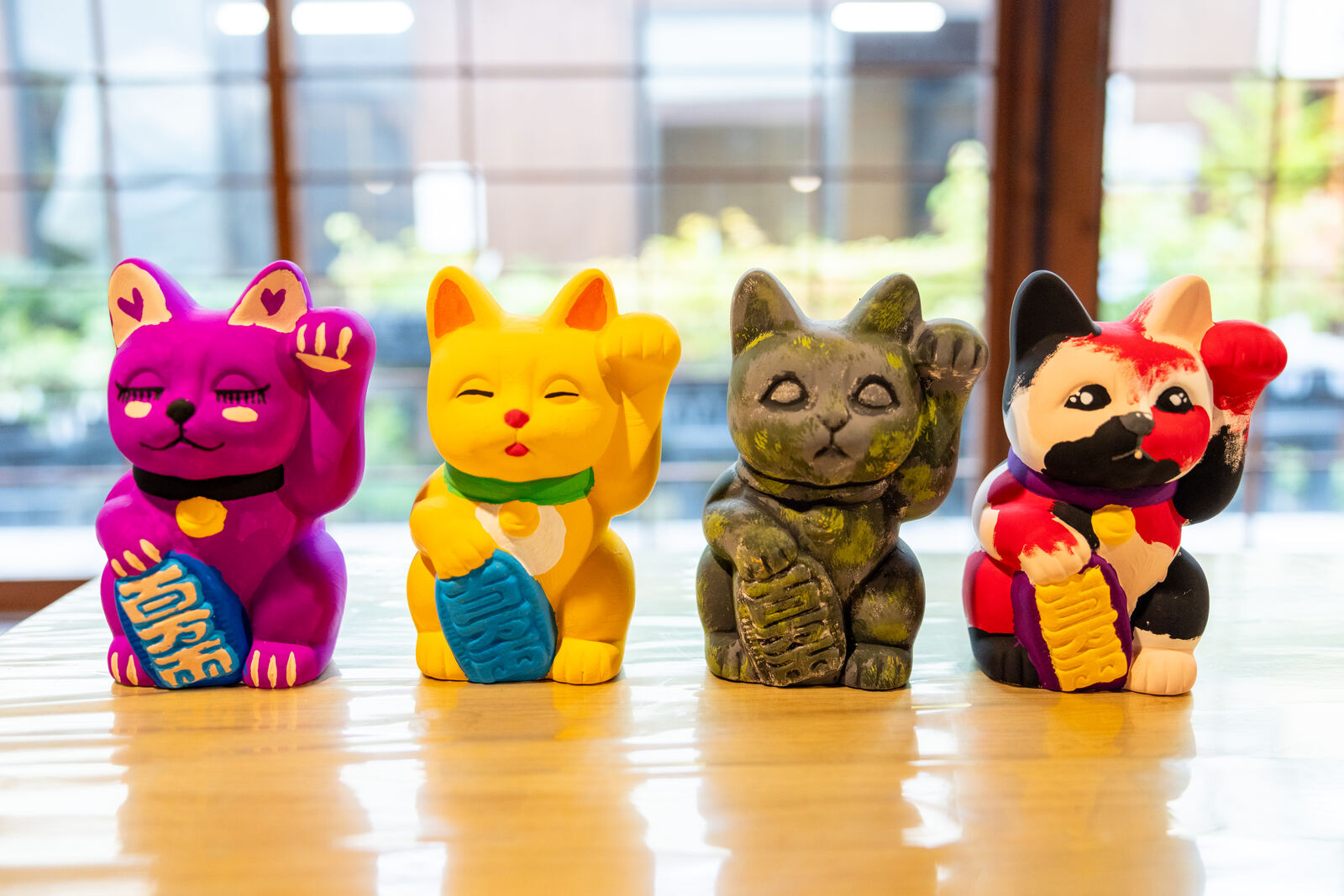 Four finished maneki-neko cats painted in different colors lined up