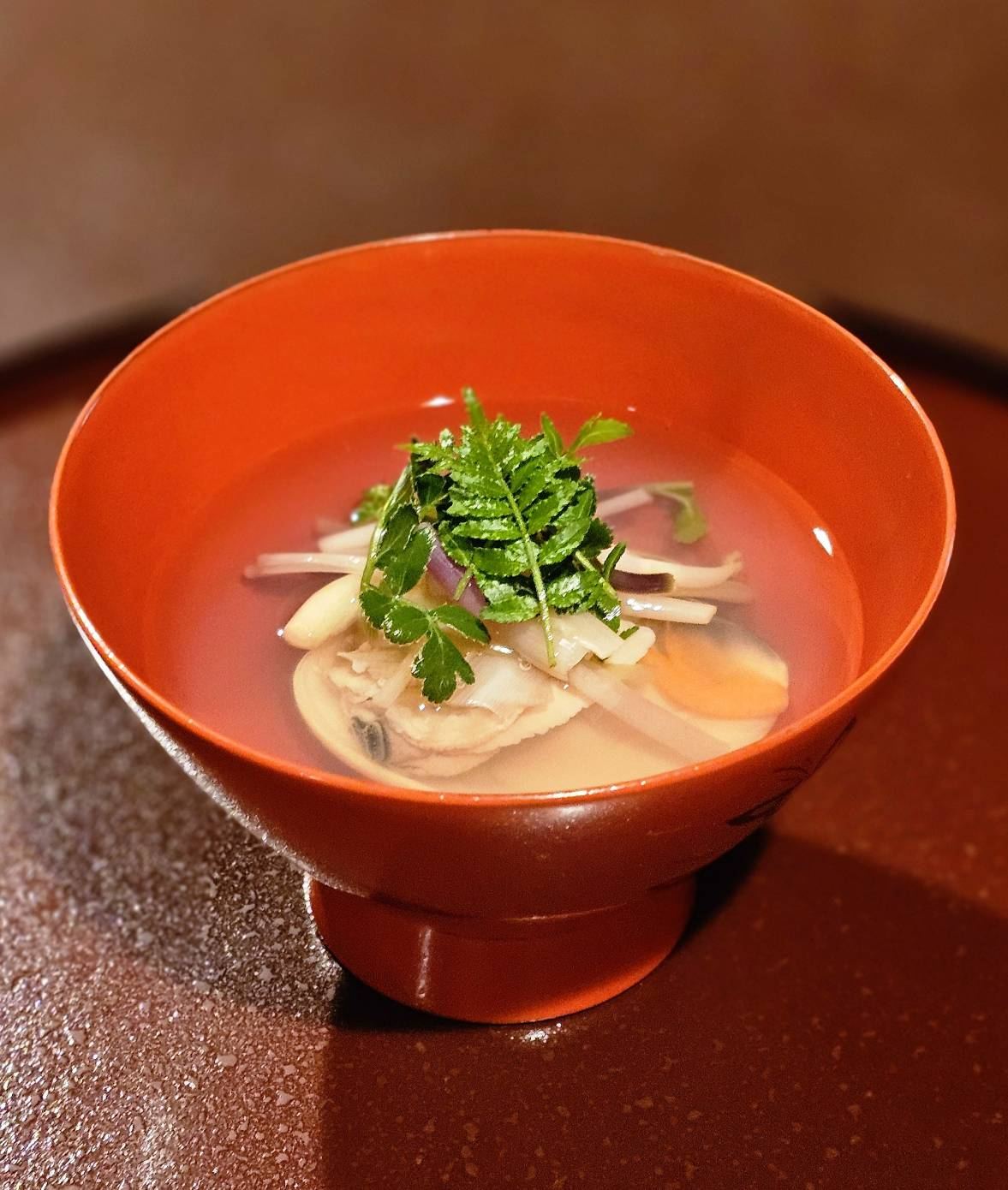 A clear clam soup served in a red lacquer bowl